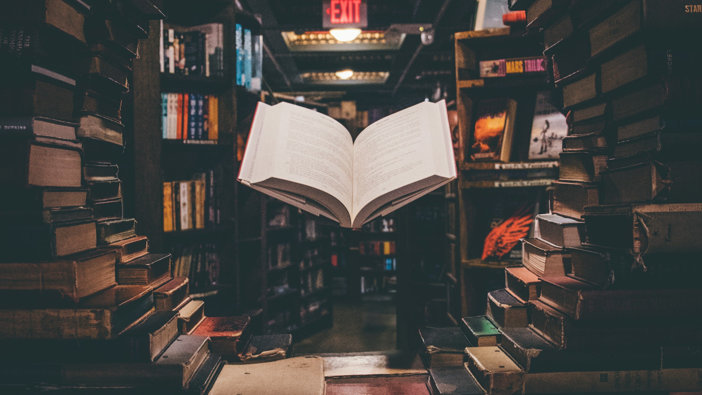 An open book floating above a stack of books in a library.